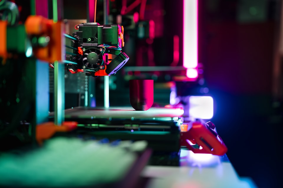 A 3D printer laying down a part under coloured workshop lighting